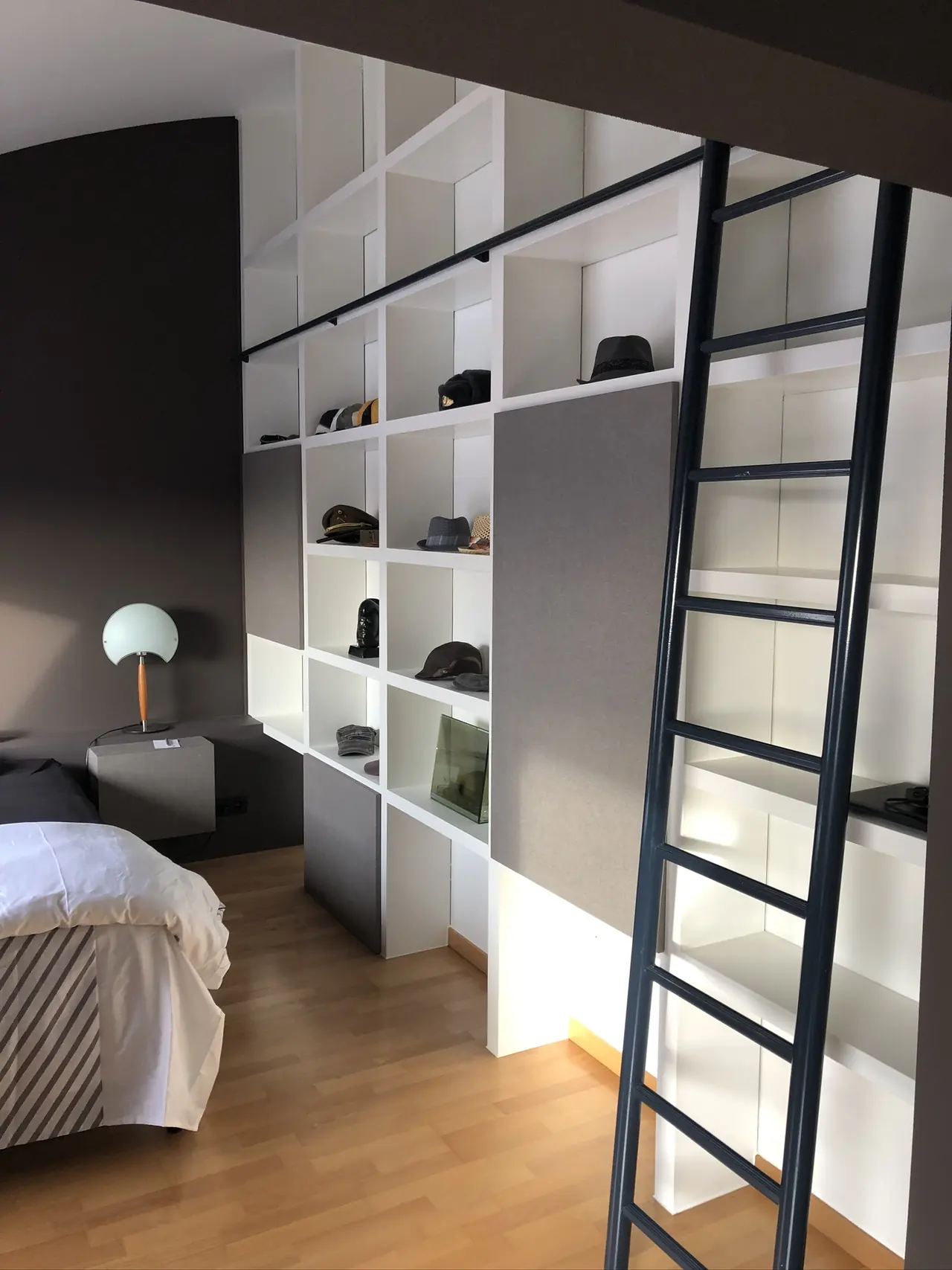Witte boekenwand op maat met zwarte bibliotheekladder in een slaapkamer