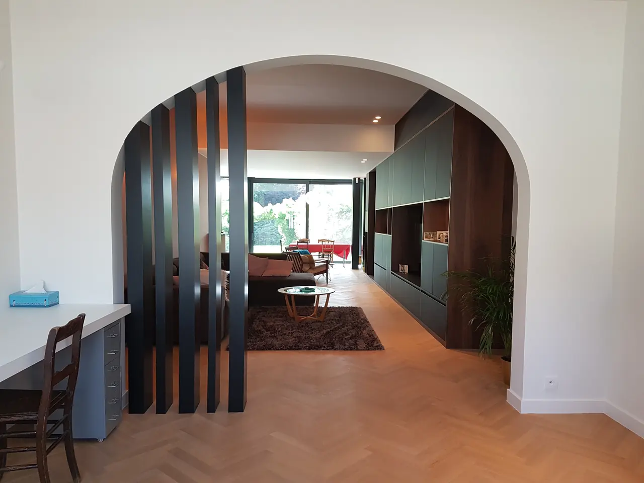 Doorkijk door een boog met donkere latten naar een maatwerk kastenwand