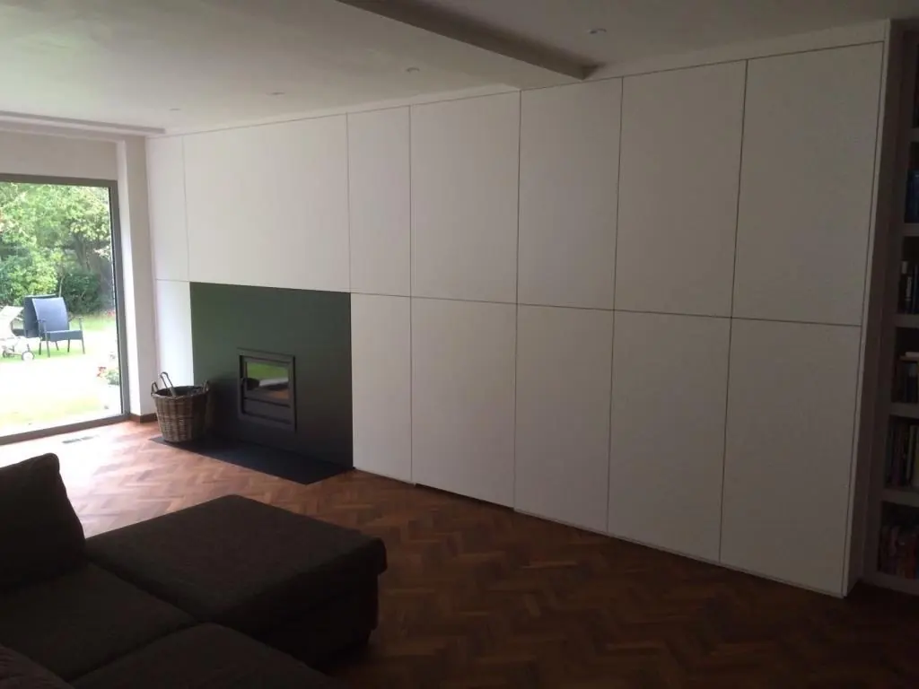 Hoge witte kastenwand met greeploze deuren in een leefruimte