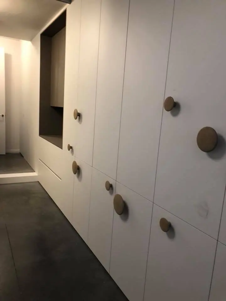 Witte greeploze kastenwand met ronde houten knoppen en een donkere nis