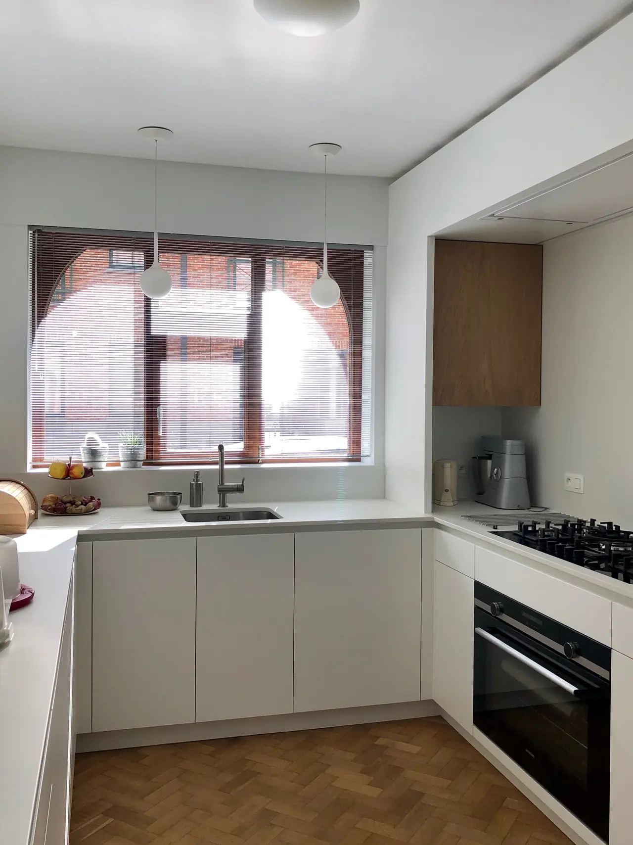 Witte U-keuken onder een raam met visgraatparket