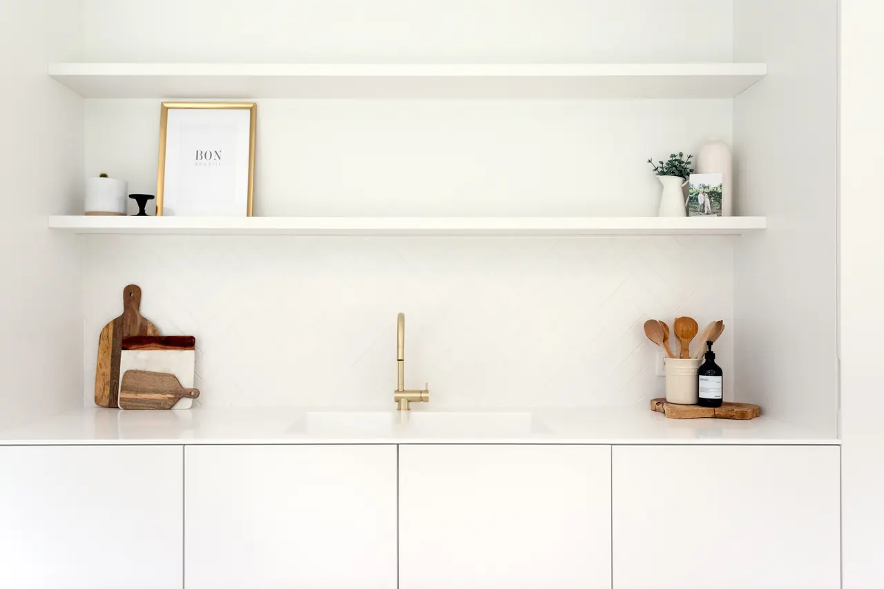 Witte kitchenette met zwevende legplanken en goudkleurige kraan